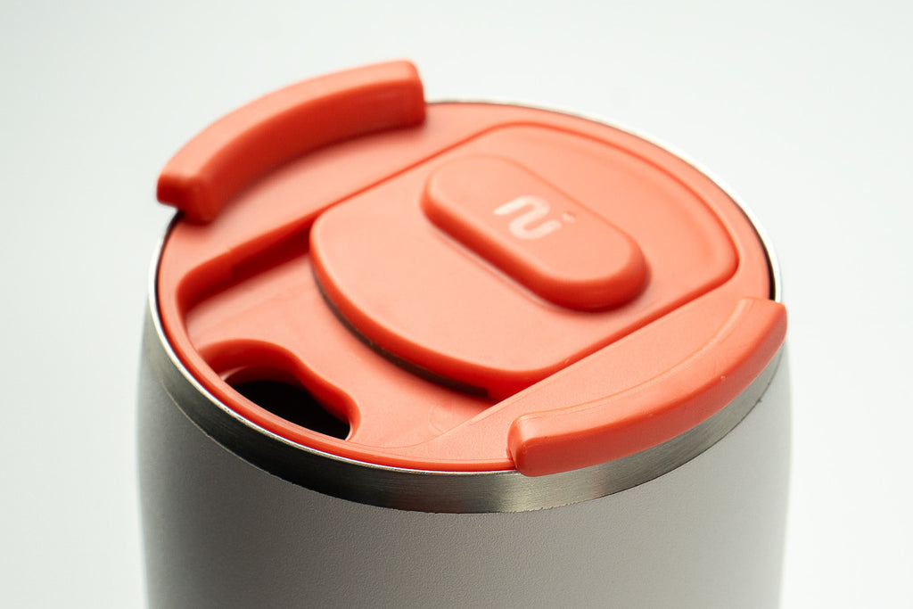 Close-up of a grey Duet coffee cup with a coral lid, on a white background.