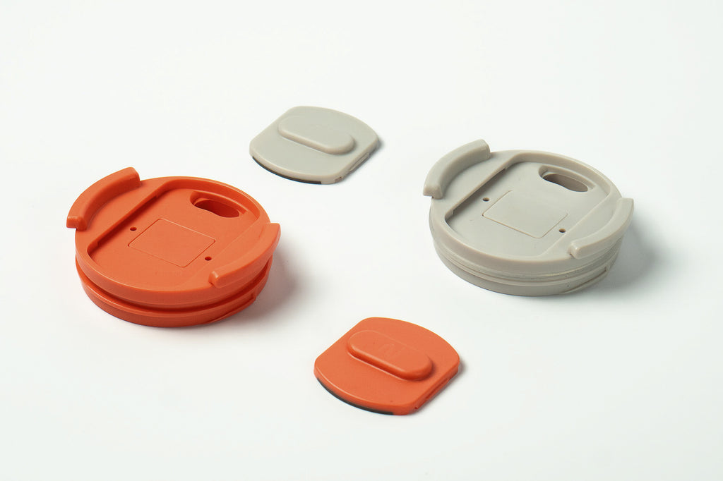 Close-up of Duet coffee cup lids and slider in coral and light grey, showing the removable slider design on a white background.