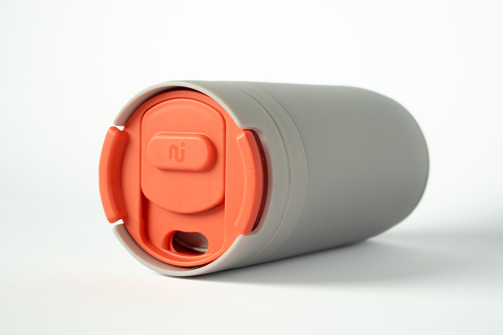 Close-up of a light grey Duet coffee cup with a coral lid stored in the base, on a white background.