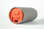 Close-up of a light grey Duet coffee cup with a coral lid stored in the base, on a white background.