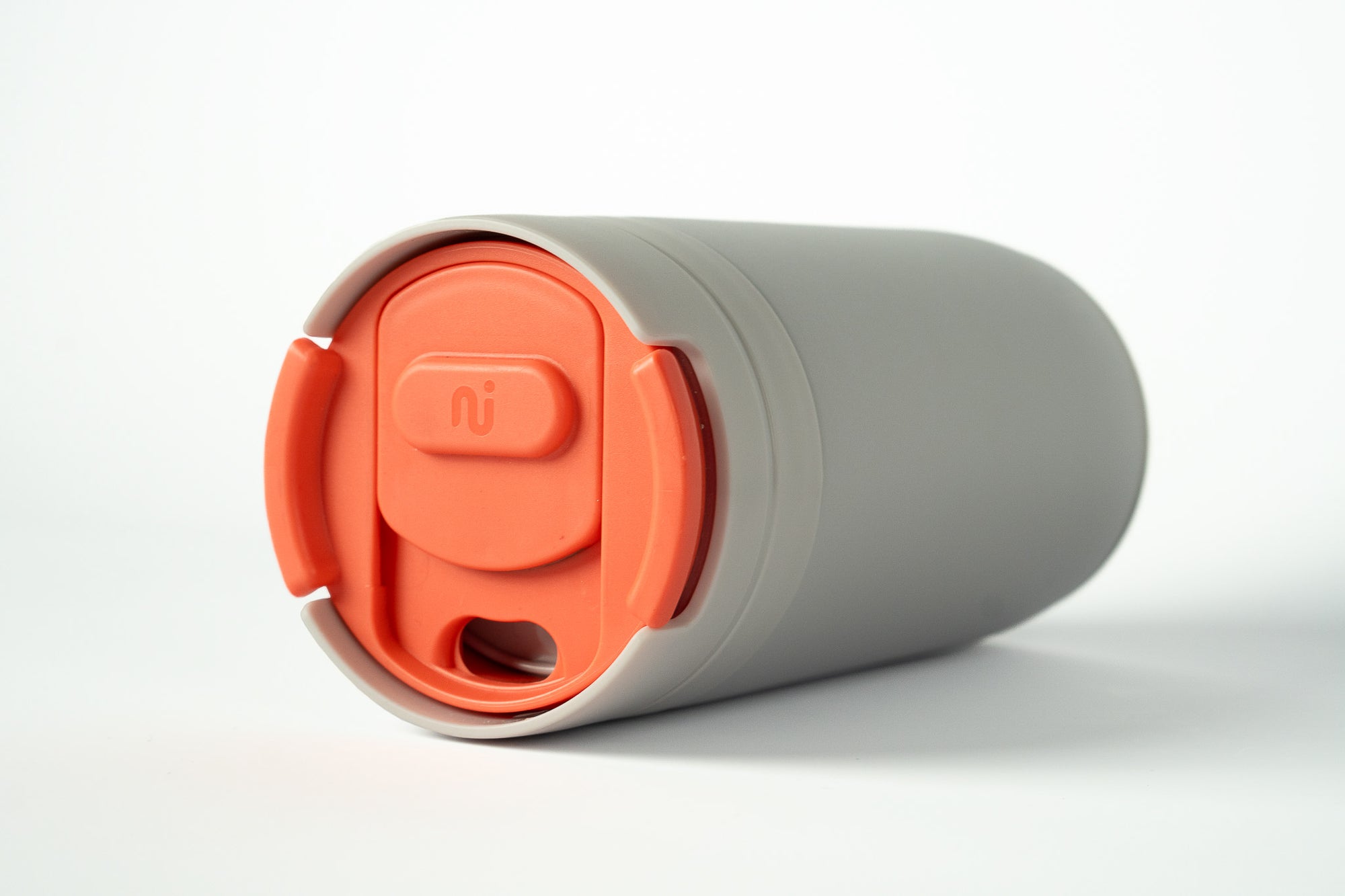 Close-up of a light grey Duet coffee cup with a coral lid stored in the base, on a white background.