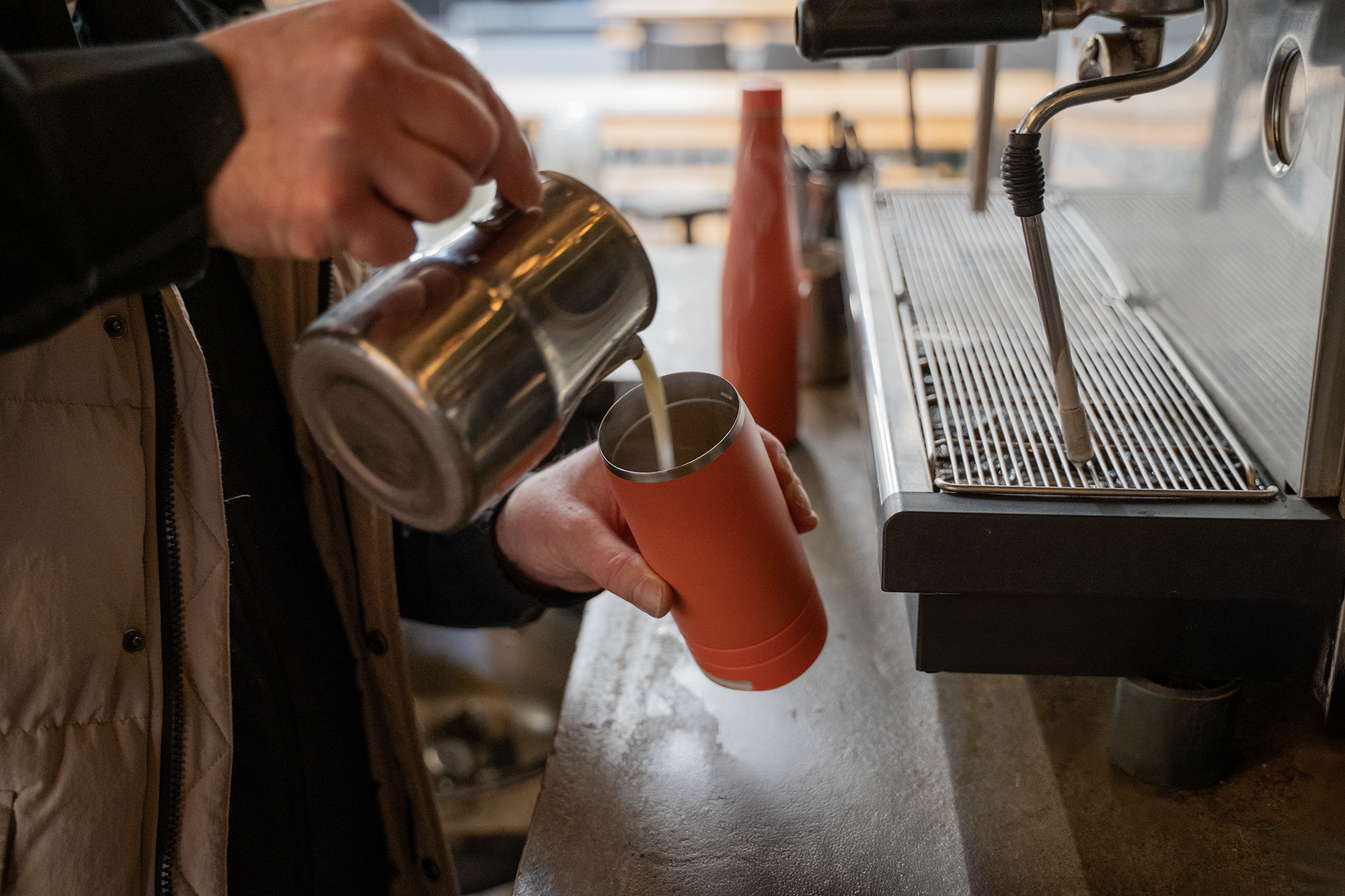 Barista pouring coffee into a coral Duet reusable coffee cup beside its matching water bottle.