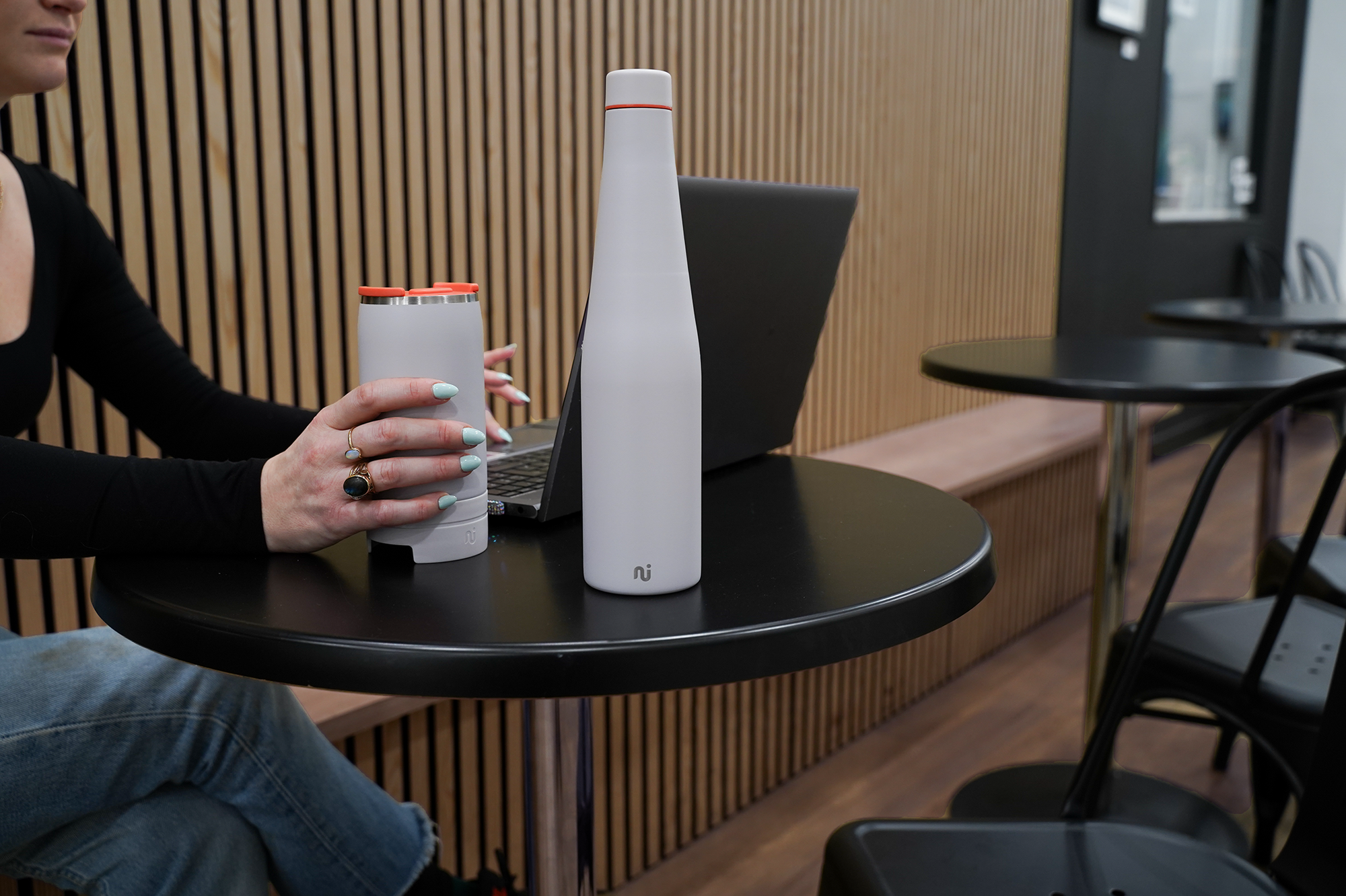 Customer drinking from a Duet coffee cup while working on a laptop, with the matching water bottle on the table.